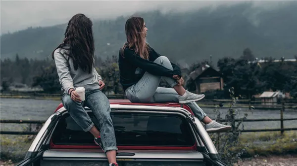 Две девушки сидят на крыше автомобиля и смотрят на небо